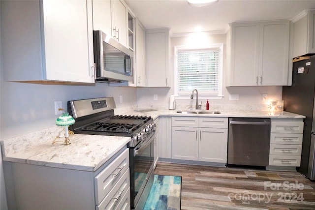 kitchen with light wood-type flooring, light stone counters, stainless steel appliances, and a sink