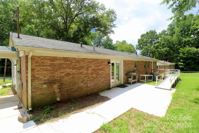 rear view of property featuring brick siding, a lawn, a patio area, and a shingled roof