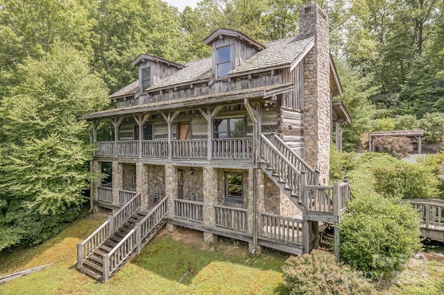 back of property with a chimney, covered porch, stairway, and stone siding