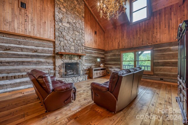 living room with hardwood / wood-style flooring, a chandelier, wooden walls, high vaulted ceiling, and a stone fireplace