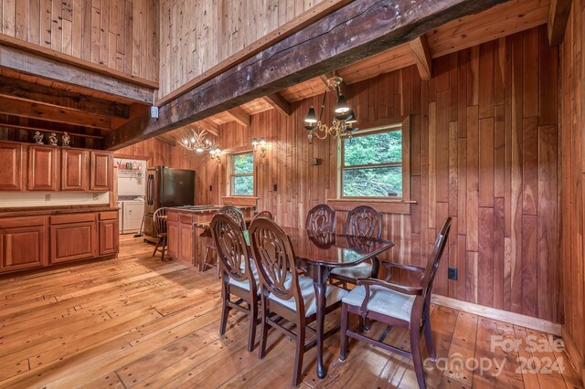 dining area featuring an inviting chandelier, beamed ceiling, wooden walls, and light hardwood / wood-style floors