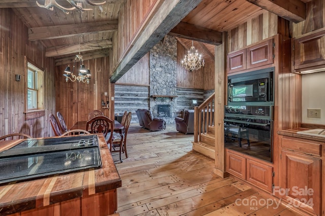 kitchen with butcher block countertops, a notable chandelier, wooden walls, and black appliances