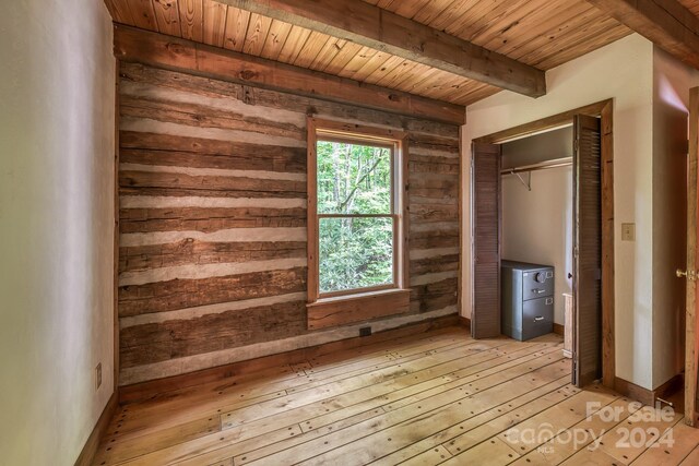 unfurnished bedroom featuring light wood-type flooring, wood walls, beamed ceiling, wooden ceiling, and a closet