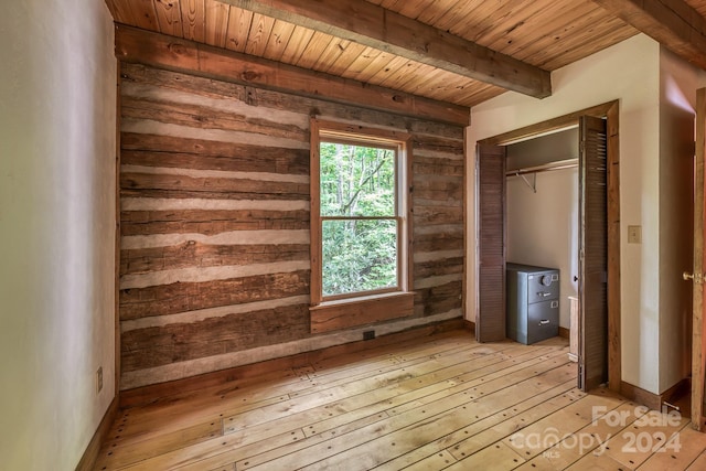 unfurnished bedroom featuring beam ceiling, light wood finished floors, a closet, wooden walls, and wooden ceiling