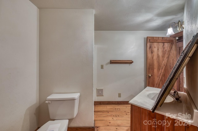 half bathroom with toilet, wood finished floors, vanity, and baseboards