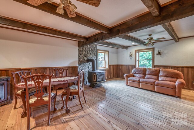 dining room featuring a wood stove, beam ceiling, ceiling fan, and light wood-type flooring