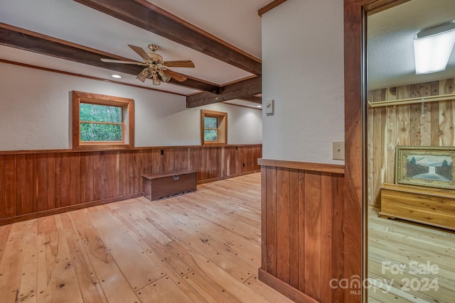 empty room with light wood-type flooring, wooden walls, beamed ceiling, and wainscoting