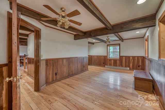 empty room featuring ceiling fan, light wood-style floors, baseboard heating, wainscoting, and beam ceiling