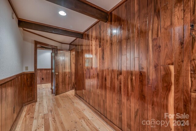 hallway with beam ceiling, light hardwood / wood-style floors, and wood walls