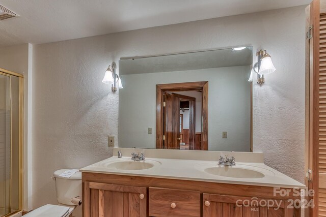 bathroom with a shower with shower door, toilet, and dual bowl vanity