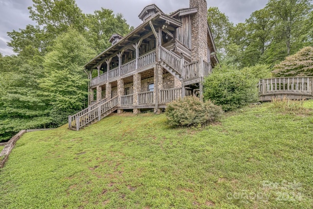 rear view of property with stone siding, a yard, stairway, a wooden deck, and a chimney