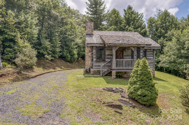 view of front of home featuring covered porch, driveway, stone siding, a chimney, and a front yard