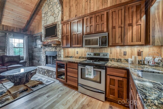 kitchen with appliances with stainless steel finishes, a fireplace, light wood-type flooring, wood walls, and wooden ceiling