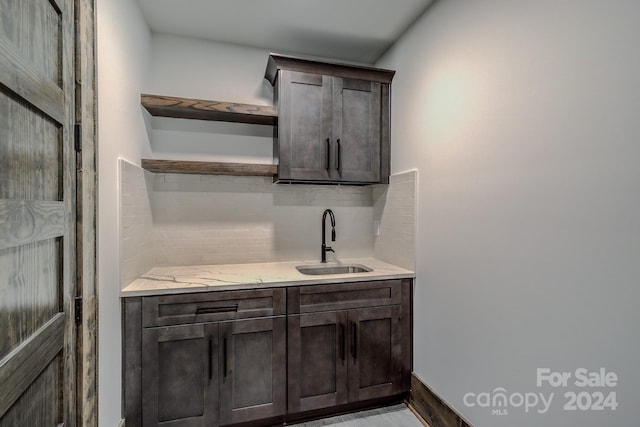 kitchen featuring light stone countertops, dark brown cabinetry, backsplash, and sink