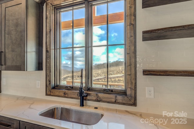 interior details with light stone counters, open shelves, backsplash, a sink, and dark brown cabinetry