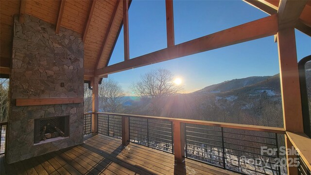 deck at dusk featuring an outdoor stone fireplace and a mountain view