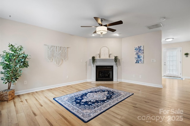 living room featuring visible vents, a fireplace with flush hearth, light wood-style flooring, baseboards, and ceiling fan