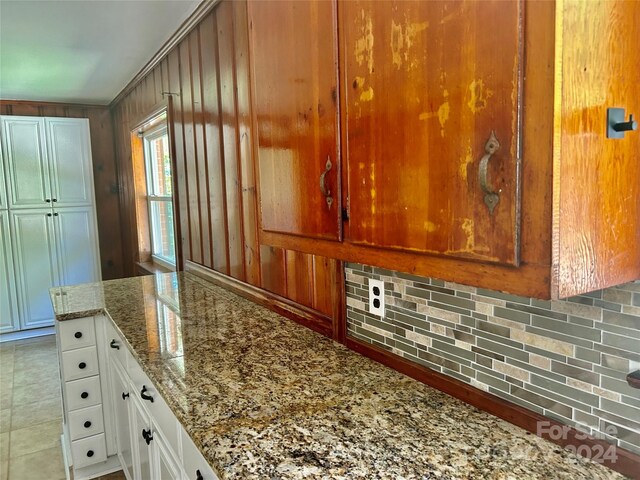 kitchen with wood walls, stone counters, tasteful backsplash, tile patterned flooring, and white cabinets