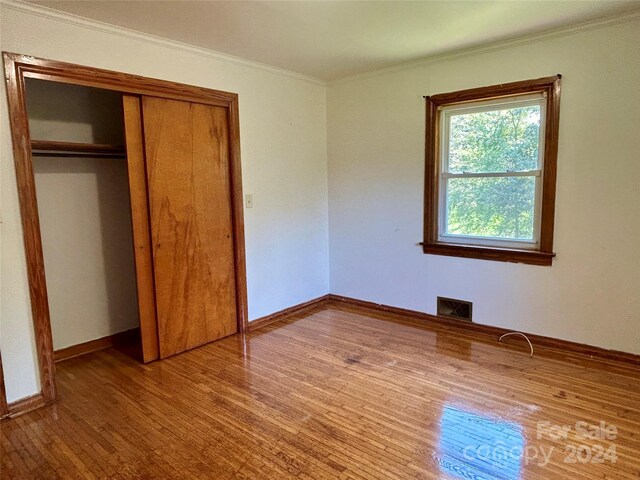 unfurnished bedroom with a closet, hardwood / wood-style floors, and ornamental molding