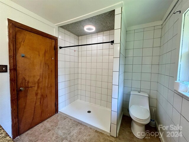 bathroom featuring tiled shower, tile patterned floors, a textured ceiling, tile walls, and toilet