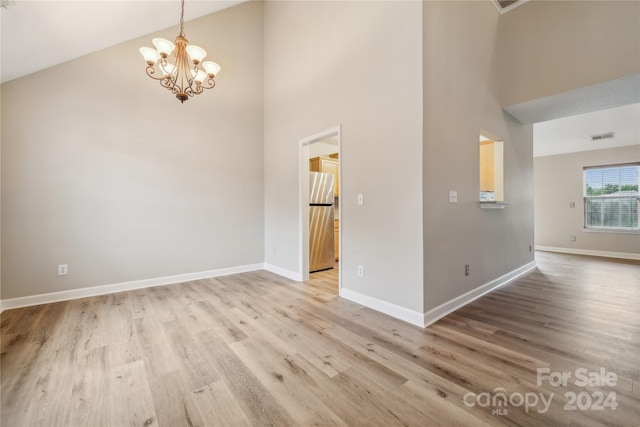 spare room featuring a notable chandelier, visible vents, a towering ceiling, wood finished floors, and baseboards