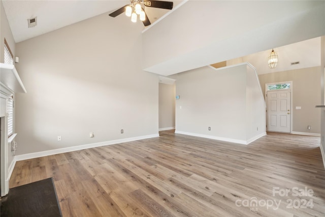 unfurnished living room featuring high vaulted ceiling, light wood-type flooring, baseboards, and ceiling fan with notable chandelier