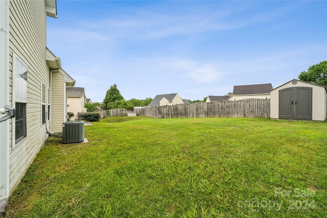 view of yard with fence, a storage unit, cooling unit, and an outbuilding