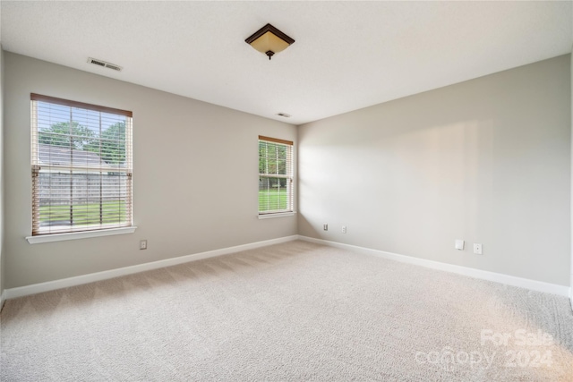 spare room with light colored carpet, plenty of natural light, visible vents, and baseboards