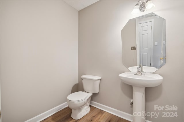 half bathroom with a sink, toilet, baseboards, and wood finished floors