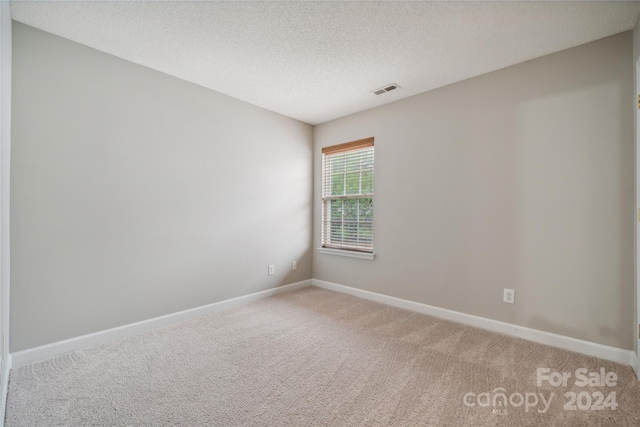 spare room with a textured ceiling, baseboards, visible vents, and light colored carpet