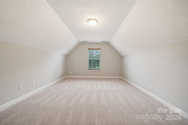 bonus room featuring lofted ceiling, baseboards, a textured ceiling, and light colored carpet