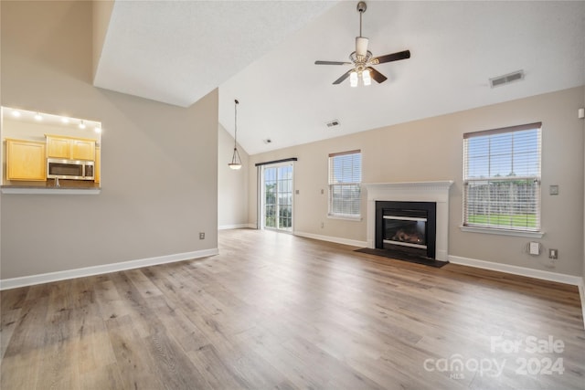 unfurnished living room with wood finished floors, a glass covered fireplace, visible vents, and baseboards