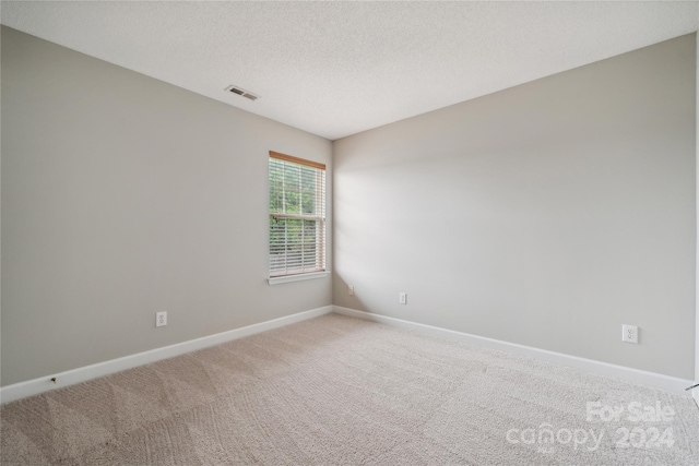 empty room with light colored carpet, visible vents, a textured ceiling, and baseboards