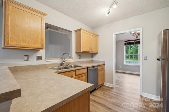 kitchen featuring stainless steel appliances, light countertops, light wood-style flooring, a sink, and a textured ceiling