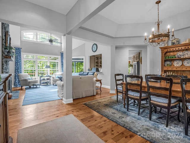 dining room with high vaulted ceiling, ceiling fan with notable chandelier, and light hardwood / wood-style flooring