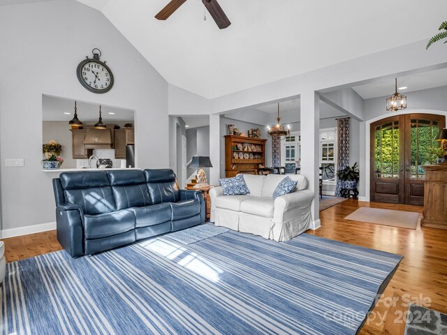 living room with high vaulted ceiling, ceiling fan with notable chandelier, hardwood / wood-style flooring, and french doors