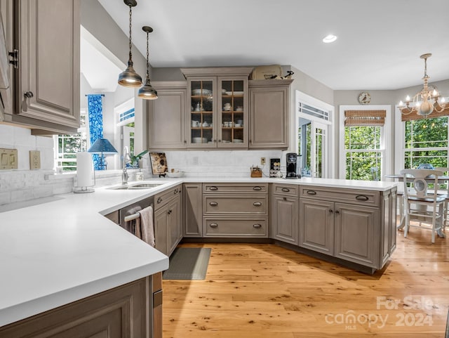 kitchen featuring an inviting chandelier, backsplash, kitchen peninsula, sink, and light wood-type flooring