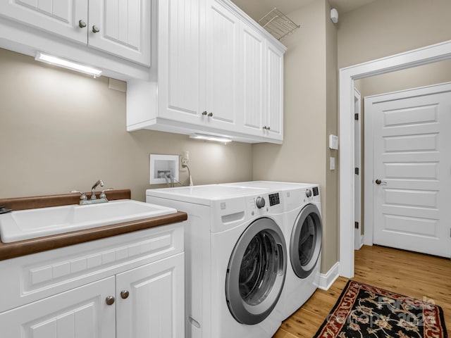 laundry room with light wood-type flooring, cabinets, washer and clothes dryer, and sink