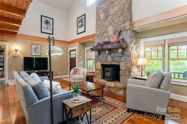 living room with baseboards, high vaulted ceiling, a wood stove, and hardwood / wood-style flooring