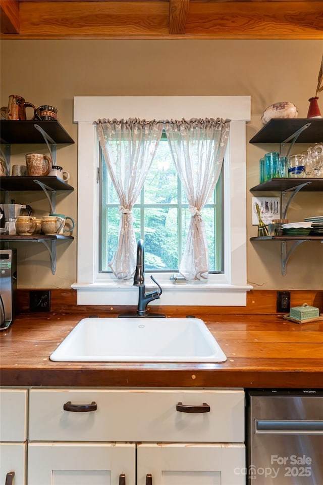 kitchen with a sink, open shelves, stainless steel dishwasher, and white cabinetry