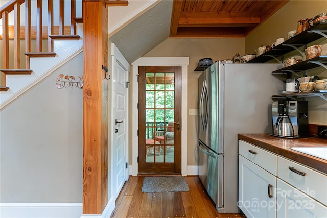 doorway featuring stairway, vaulted ceiling with beams, light wood-style floors, and baseboards