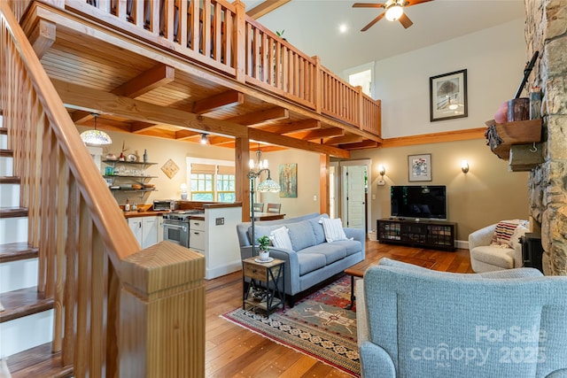 living room with light wood finished floors, stairway, beamed ceiling, ceiling fan with notable chandelier, and a high ceiling