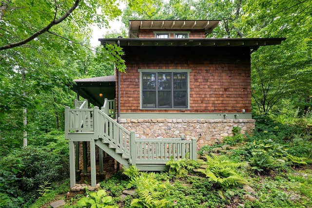 view of home's exterior with a wooden deck, stone siding, and stairs