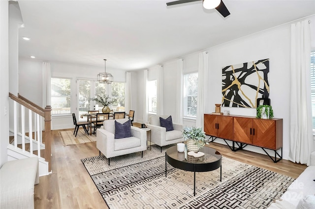 living room with ceiling fan with notable chandelier, wood-type flooring, and a healthy amount of sunlight