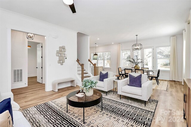 living room with light wood-type flooring and ceiling fan with notable chandelier