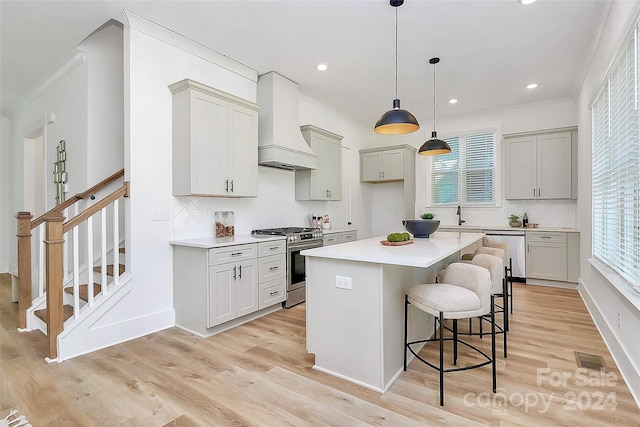 kitchen with appliances with stainless steel finishes, light hardwood / wood-style floors, a kitchen island, and premium range hood