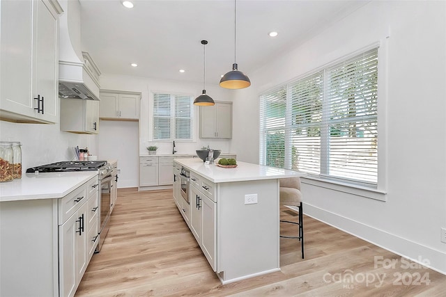 kitchen featuring premium range hood, a kitchen island, stainless steel stove, decorative light fixtures, and light hardwood / wood-style floors