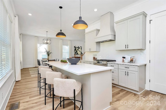 kitchen with light wood-type flooring, a kitchen bar, hanging light fixtures, and custom exhaust hood