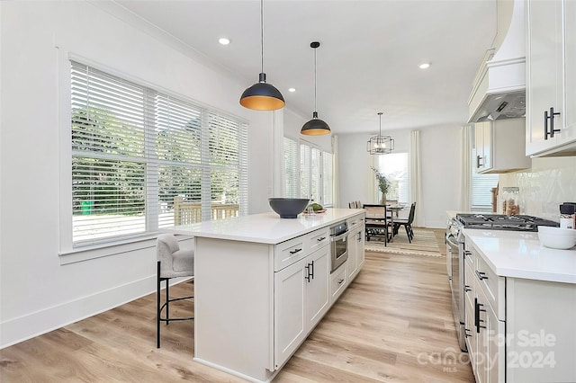 kitchen with stainless steel appliances, white cabinetry, decorative light fixtures, light hardwood / wood-style flooring, and a center island