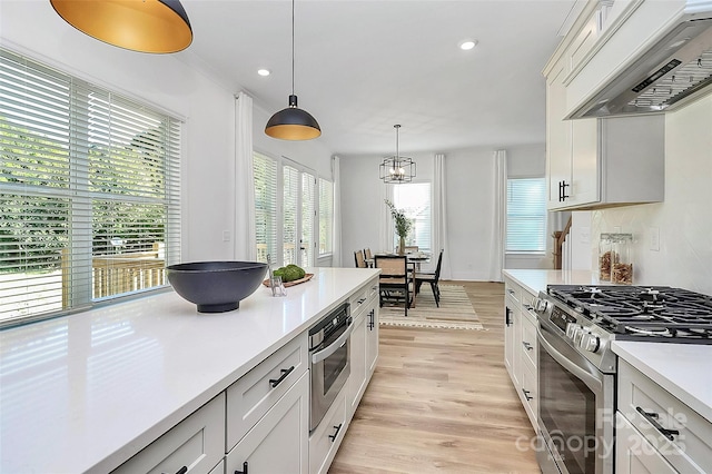 3230 Rogers St, Charlotte, NC 28208 - kitchen with light countertops, light wood finished floors, gas stove, hanging light fixtures, and wall chimney range hood